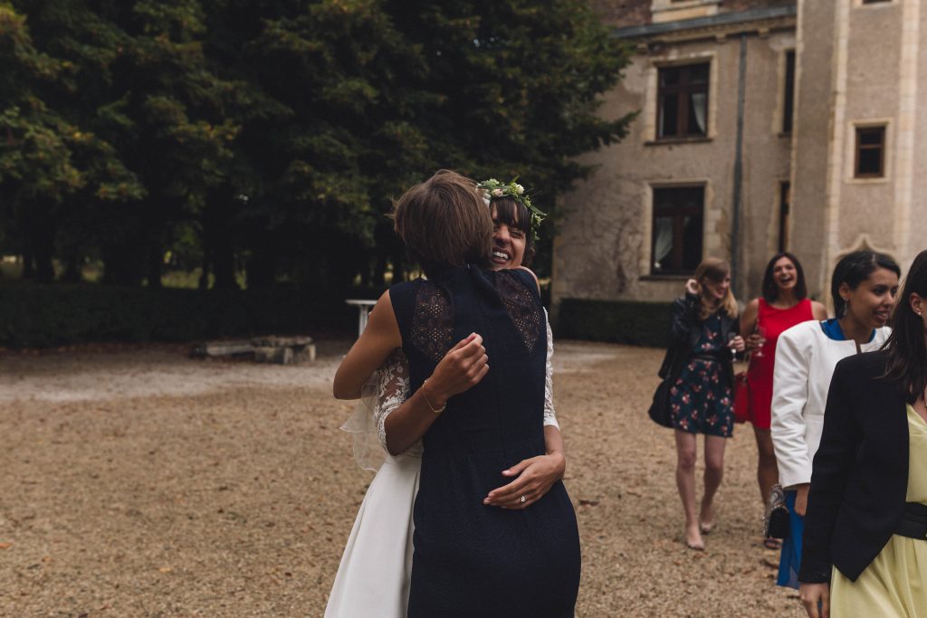 La mariée à la couronne de fleurs serrant une invitée dans la cour de gravier d'un château de la Nièvre