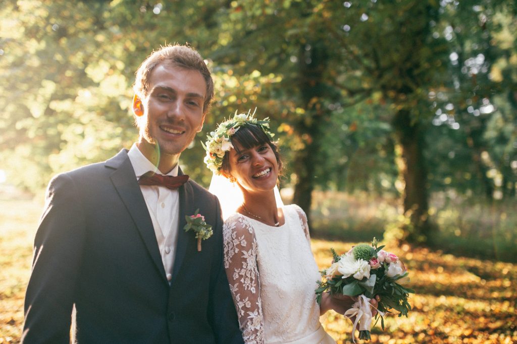 Les mariés dans un sous-bois à contre-jour, la mariée à la couronne de fleurs et au bouquet champêtre