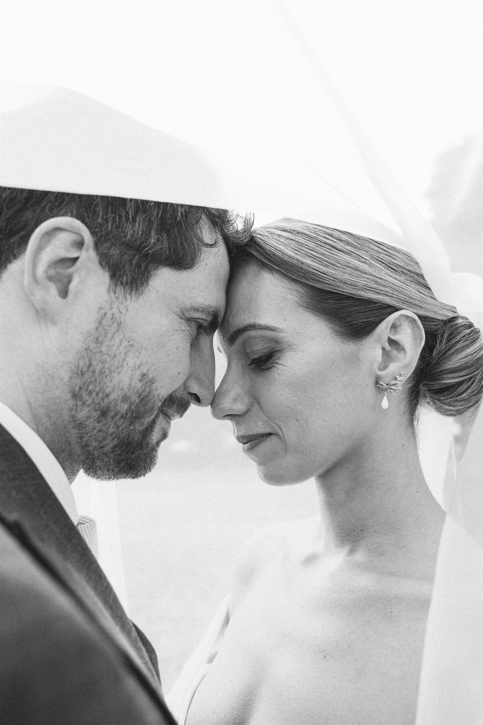 Les mariés front contre front sous le voile, photographie de mariage en noir et blanc