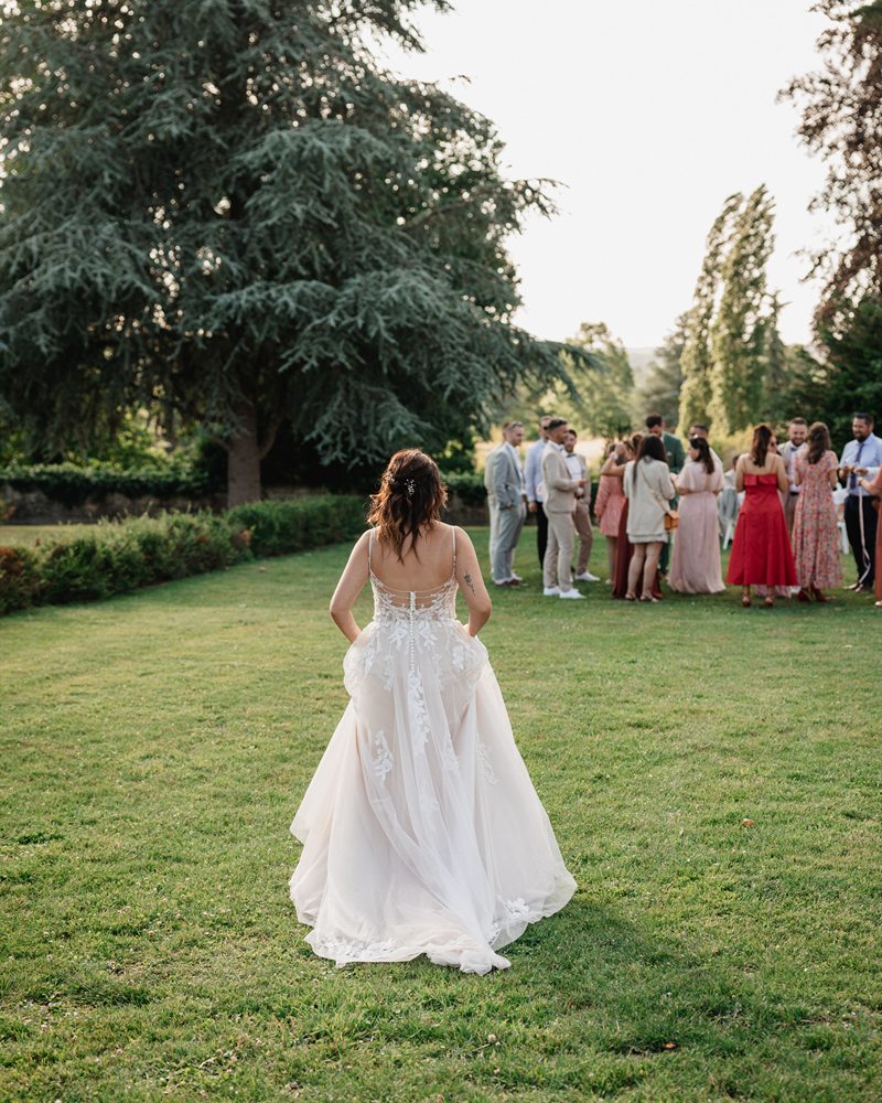 Mariée de dos en robe de bal traversant le parc vers ses invités