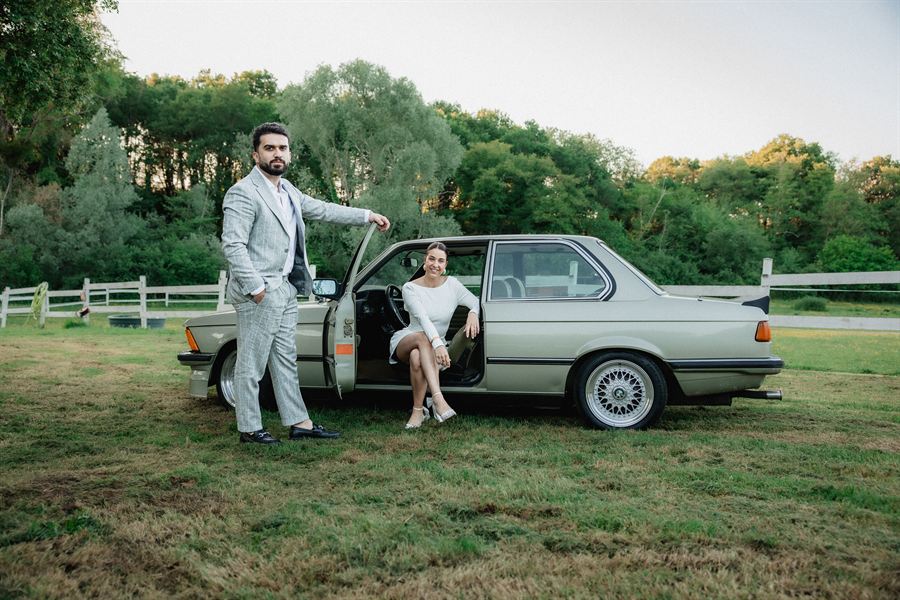 Les mariés devant une BMW ancienne, à la lumière du soir