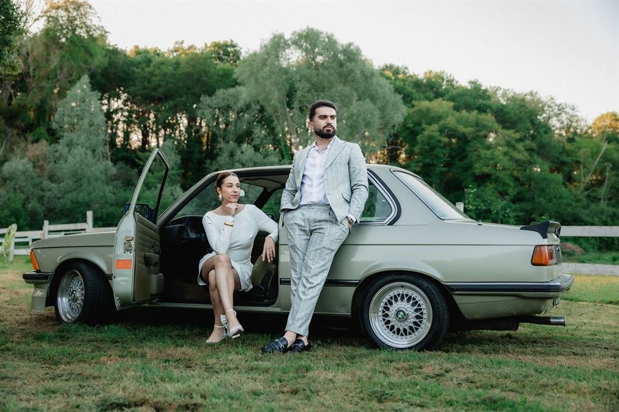 La mariée assise dans une BMW ancienne, le marié à ses côtés