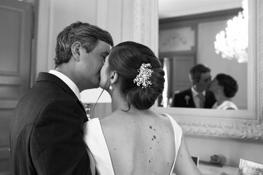 Les mariés s’embrassant devant un miroir doré, salon de château, noir et blanc
